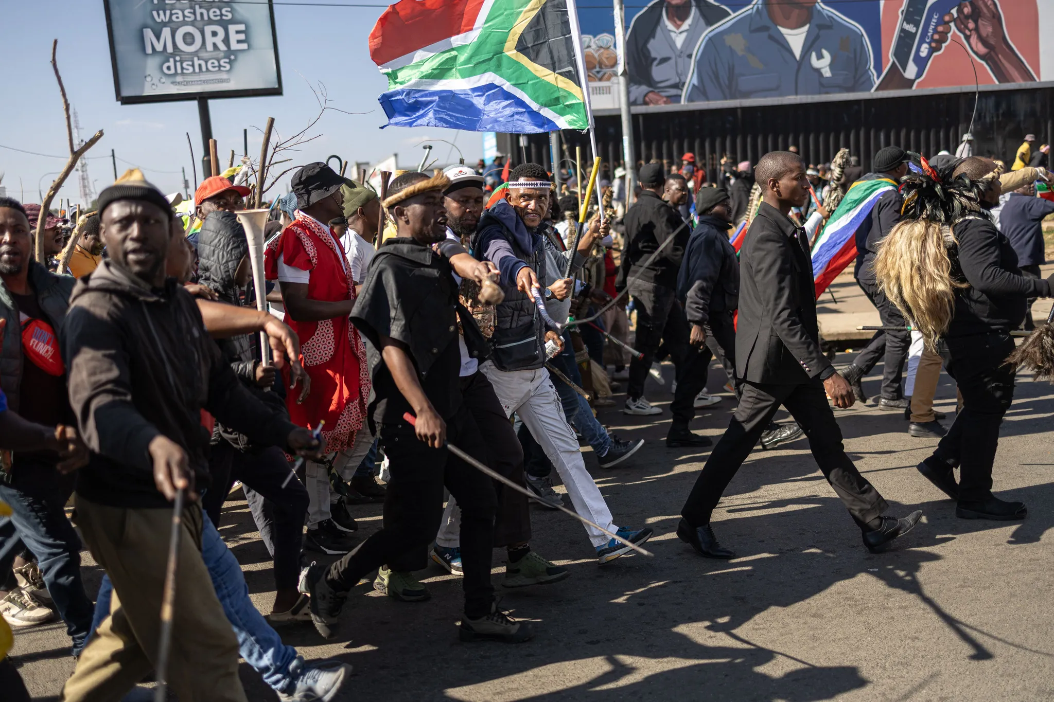 Manifestants brandissant le drapeau national pour dénoncer la présence des étrangers, rappelant le contexte difficile pour une coiffeuse en Afrique du Sud.